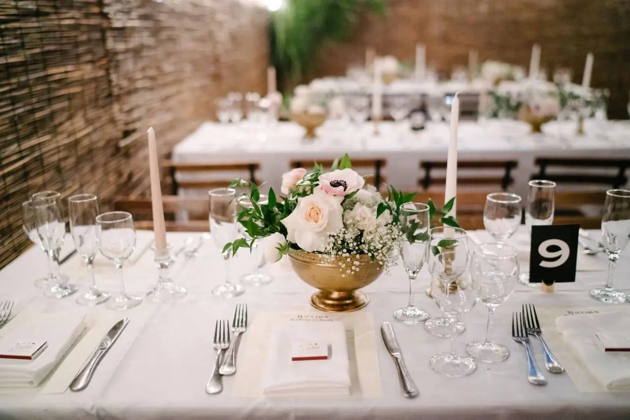 A table set with white and gold plates, candles, and flowers.