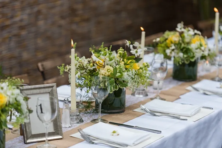 A table set with candles and flowers on top of burlap.