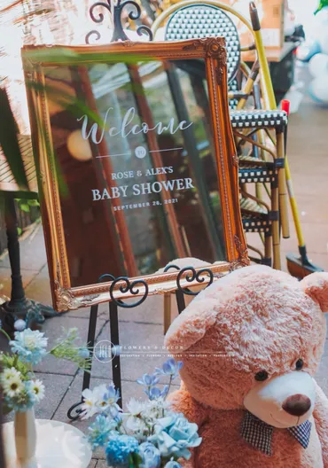 A teddy bear sitting in front of a baby shower sign.